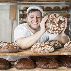 Bäcker Nick in seiner Backstube hält ein rundes, frisch gebackenes Brot.